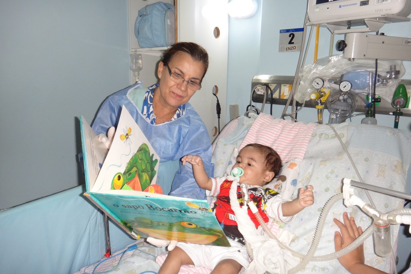 Voluntária mostra as figuras do livro para o bebê internado. Foto Divulgação