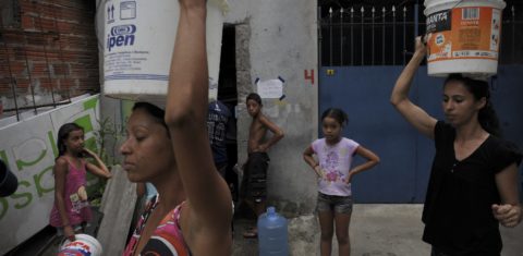 Mulheres carregam baldes na cabeça na favela de Paraisópolis, em São Paulo: acesso a água precisa ser universalizado. Foto Maurício Lima/AFP