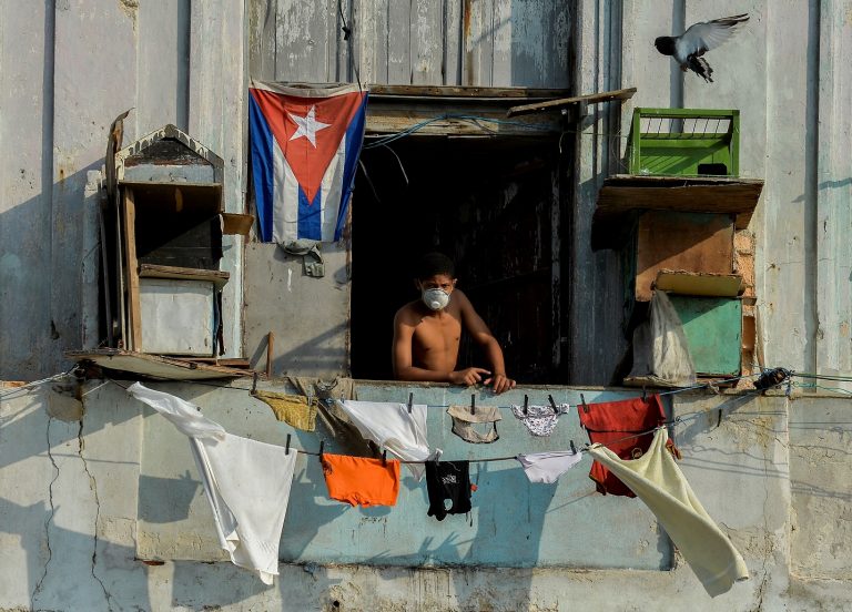 Homem usa máscara facial na varanda em Havana. As autoridades cubanas dizem que o embargo econômico dos EUA vem dificultando o combate à covid-19. Foto Yamil Lage/AFP
