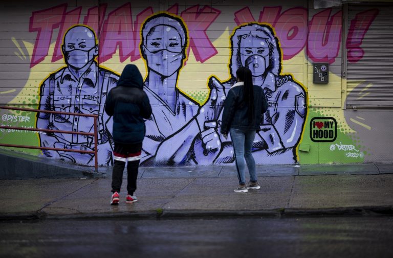 Duas mulheres no Harlem, em Nova York, observam o mural do artista @Dister, retratando socorristas com máscaras e uma mensagem de agradecimento. Foto Johannes Eisele/AFP