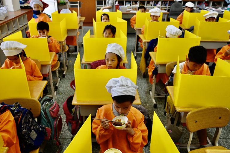 Em Taiwan, alunos almoçam em mesas com divisórias plásticas como medida preventiva para conter a disseminação da covid-19. Foto Sam Yeh/AFP