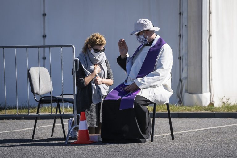 Padre usando máscara contra a covid-19 ouve a confissão de uma fiel em frente a uma igreja em Varsóvia, na Polônia. Foto Wojtek Radwanski/AFP