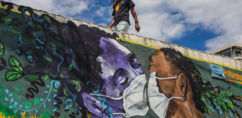Um homem usando máscara passa por um grafite do artista Marcos Costa, ou Spraycabuloso, na entrada da favela Solar de Unhão, em Salvador. Foto Antonello Veneri/AFP