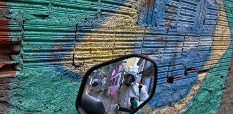 Um homem é refletido no espelho de uma motocicleta enquanto desinfeta uma área dentro da favela de Babilônia,na Zona Sul do Rio de Janeiro. Foto Carl de Souza/AFP