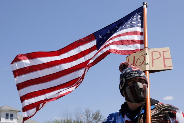 Um homem segura a bandeira dos EUA em protesto contra o barbeiro Karl Manke, que abriu sua loja apesar das ordens de fechamento no estado Michigan. Foto Jeff Kowalsky/AFP