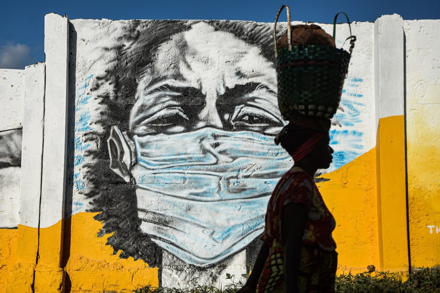 Na Tanzânia, uma mulher carrega uma cesta na cabeça enquanto caminha em frente a um grafite pintado pelo grupo de artistas Wachata para aumentar a conscientização sobre o uso de máscaras na pandemia. Foto Ericky BONIPHACE / AFP