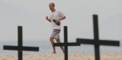 Banhista corre na praia de Copacabana em meio às cruzes plantadas pela ONG Rio de Paz em protesto contra a política de combate ao covid-19 na cidade e no país. Foto Dikran Junior/AGIF