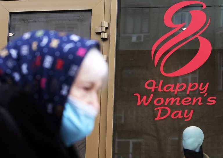 Em Kiev, na Ucrânia, mulher passa com máscara de proteção contra a covid-19 diante de um cartaz em comemoração ao Dia Internacional da Mulher. Foto STR/NurPhoto/AFP