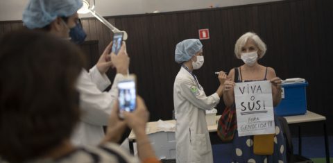 Ao ser vacinada no Planetário, no Rio de Janeiro, mulher segura um cartaz celebrando o trabalho do SUS e criticando o presidente Jair Bolsonaro. Foto Mauro Pimentel/Março/2021