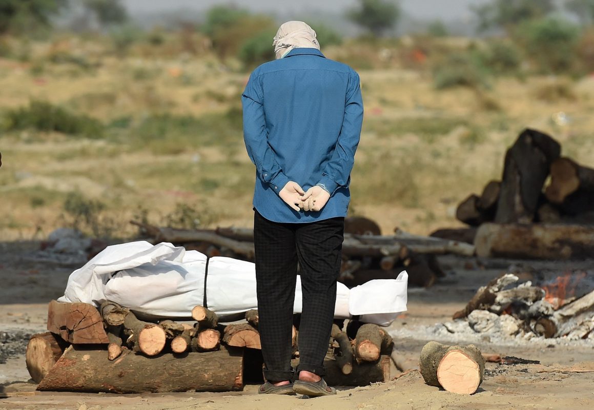 Foto Sanjay Kanojia/AFP. Maio/2021 Em um campo de cremação, em Allahabad, na Índia, parente chora ao lado do corpo de seu ente querido que morreu devido à Covid-19. Foto Sanjay Kanojia/AFP. Maio/2021