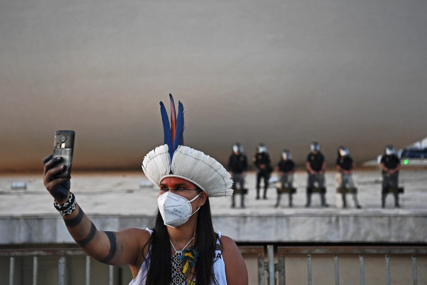 Brasil, América do Sul: mulher indígena, usando máscara contra a covid-19, tira selfie em frente à tropa de choque no prédio do Supremo Tribunal Federal, em Brasília. Foto Carl de Souza/AFP. Agosto/2021