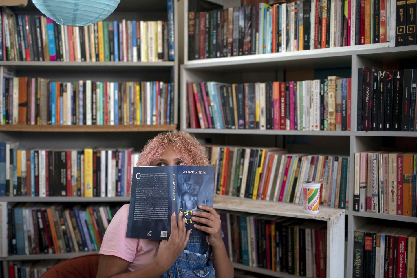 A jovem Lua Oliveira, de 12 anos, espia por trás de um livro na biblioteca pública Mundo da Lua, fundada por ela na favela dos Tabajaras, no Rio de Janeiro. Um bom exemplo de resistência. Foto Mauro Pimentel/AFP