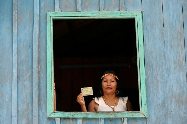 Indígena Kambeba mostra o título de leitor da janela de casa, à beira do Rio Negro, no Amazonas. Foto Michael Dantas/AFP