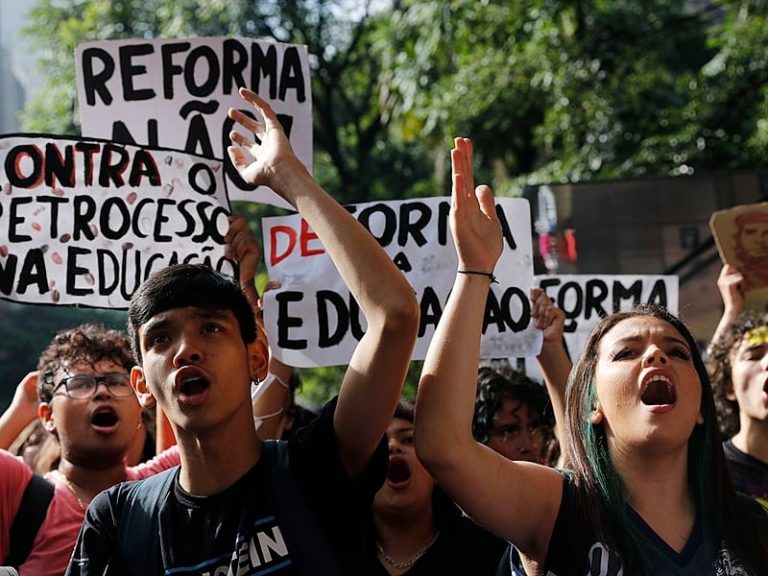 Foto colorida de estudantes em manifestação pela revogação do novo ensino médio. Na foto, jovens aparecem com cartazes e os braços levantados, enquanto gritam