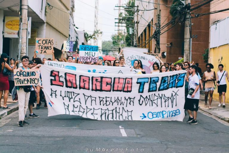 Foto colorida de estudantes segurando faixa durante marcha da consciência trans em Campinas. Movimento foi idealizado para buscar cotas para pessoas trans na Universidade