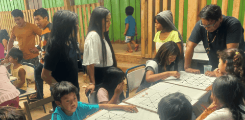 Foto colorida de estudantes durante atividade do abril indígena na escola indígena Augusto Ope da Silva. Os estudantes diante de uma mesa, outros ao redor.