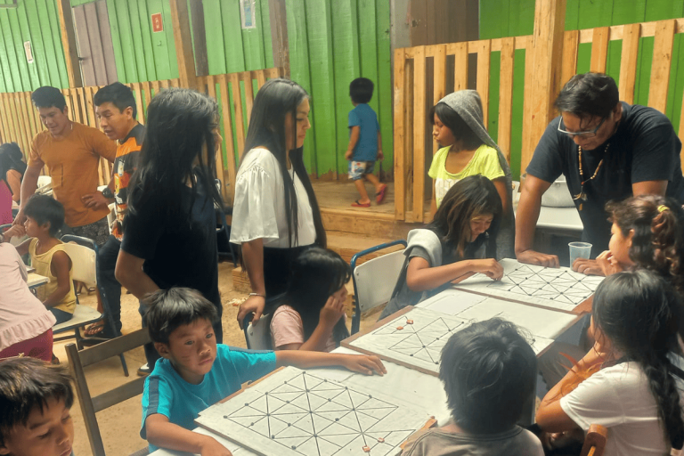 Foto colorida de estudantes durante atividade do abril indígena na escola indígena Augusto Ope da Silva. Os estudantes diante de uma mesa, outros ao redor.