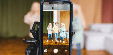 Foto colorida de uma tela de celular posicionada para filmar crianças em pé. Prática de sharenting pode expor menores de idade