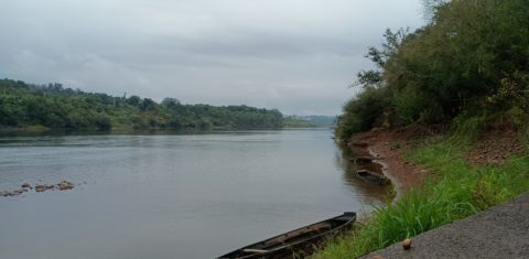 Foto colorida do Rio Taquari, em Arroio do Meio. Na imagem, está nublado e aparece uma canoa próxima da margem do Rio