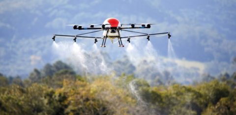 Foto colorida de drone pelicano lançando agrotóxicos. O drone está no alto e abaixo dele aparecem jatos com líquido caindo. Emergência química no Maranhão