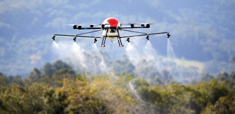Foto colorida de drone pelicano lançando agrotóxicos. O drone está no alto e abaixo dele aparecem jatos com líquido caindo. Emergência química no Maranhão