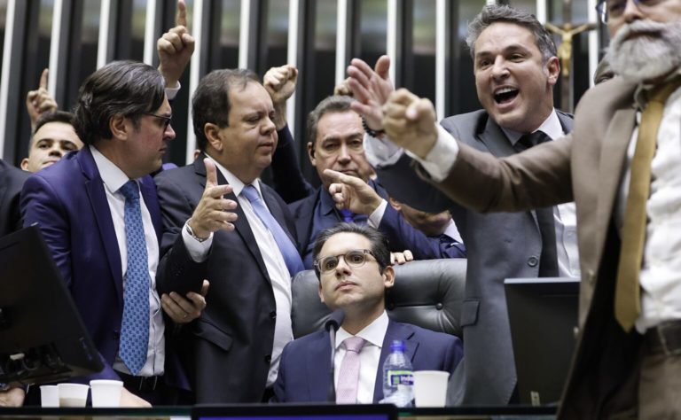 Foto colorida que mostra o deputado Hugo Motta, sentado no plenário da Câmara e cercado por deputados da direita; bancada ruralista se articulou para atacar legislação ambiental