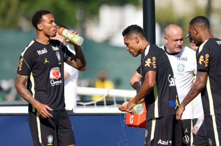 Foto colorida de Gabriel Magalhães e Alex Sandro, jogadores de futebol da seleção brasileira, bebendo água durante treino nos Estados Unidos