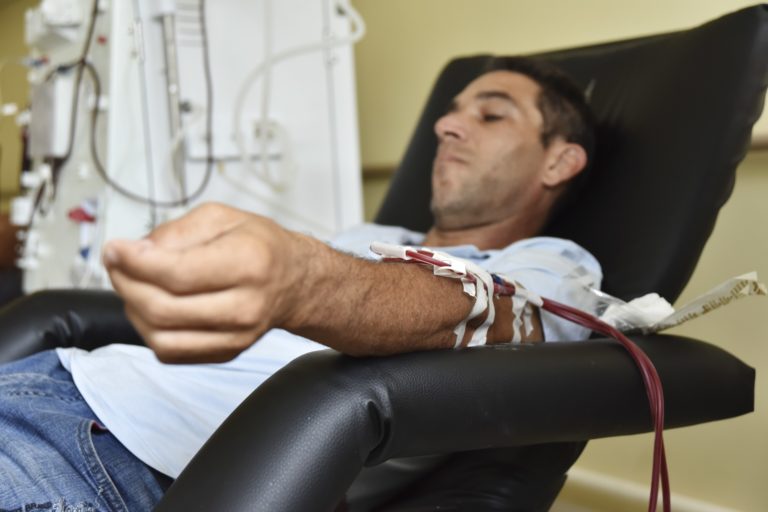 Foto colorida de pessoa recebendo transfusão de sangue. Ele é um homem branco, com cabelo curto preto, está sentado em uma cadeira no Centro de Hemodiálise do Hospital Regional de Sobradinho (HRS), no Distrito Federal.