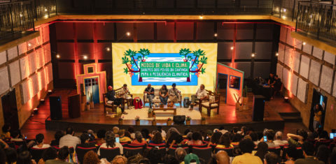 Foto colorida do painel: Modos de vida e clima, que abriu os debates da segunda edição da semana do clima na Caatinga, no Cais do Sertão, em Recife. Na imagem, aparecem os painelistas no centro e o público de costas, assistindo o evento.