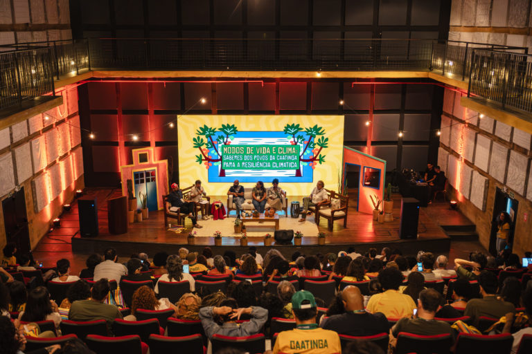Foto colorida do painel: Modos de vida e clima, que abriu os debates da segunda edição da semana do clima na Caatinga, no Cais do Sertão, em Recife. Na imagem, aparecem os painelistas no centro e o público de costas, assistindo o evento.